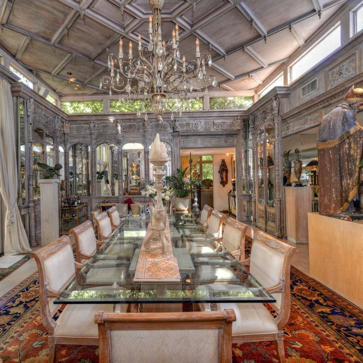 A spacious dining room with a long glass table, surrounded by chairs, and adorned with various sculptures and decorative elements.