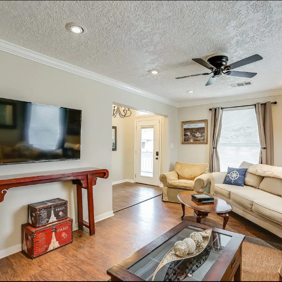 A living room with a television mounted on the wall, a sofa, a coffee table, and a door leading outside.