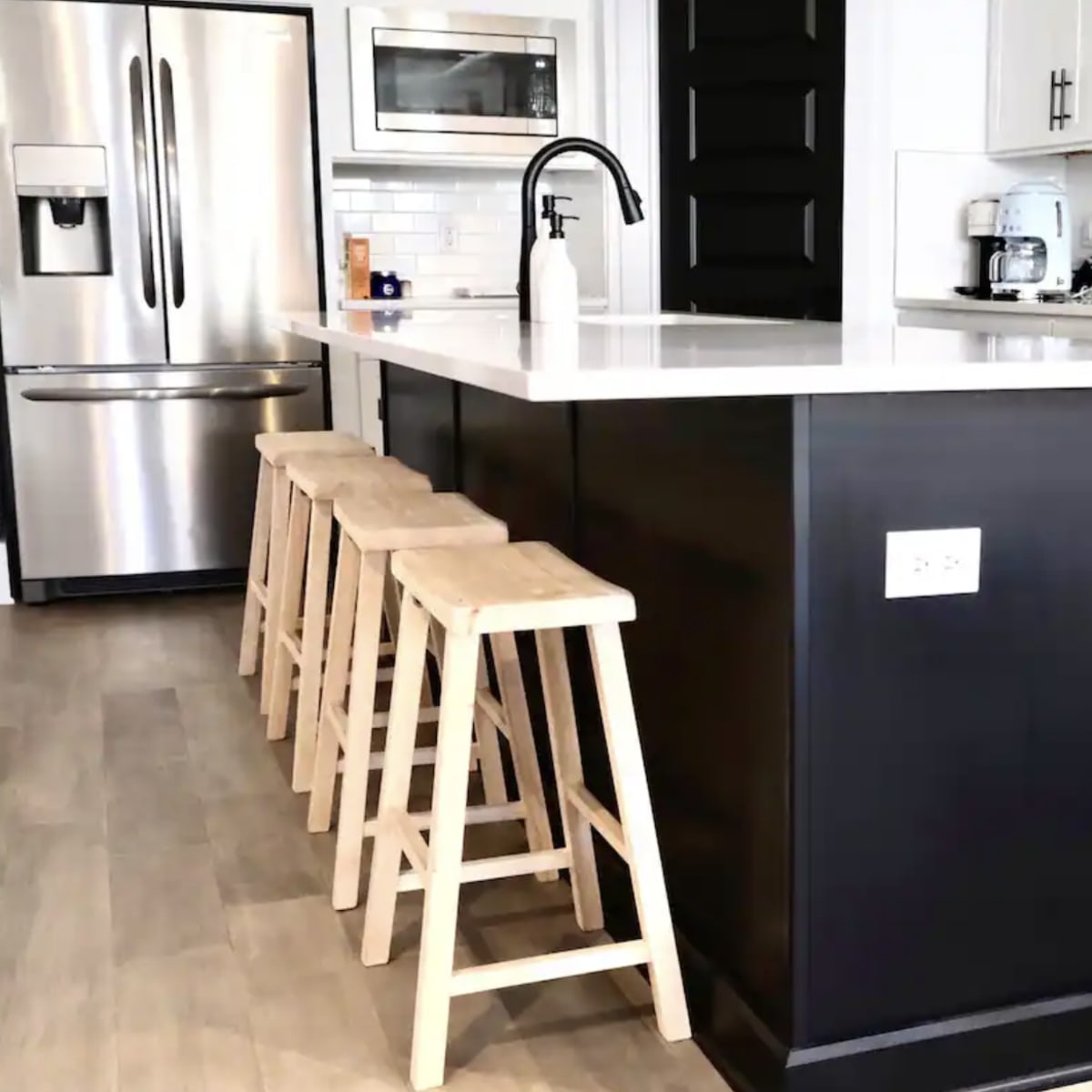 A modern kitchen with a black island, three wooden stools, stainless steel appliances, and white cabinetry.
