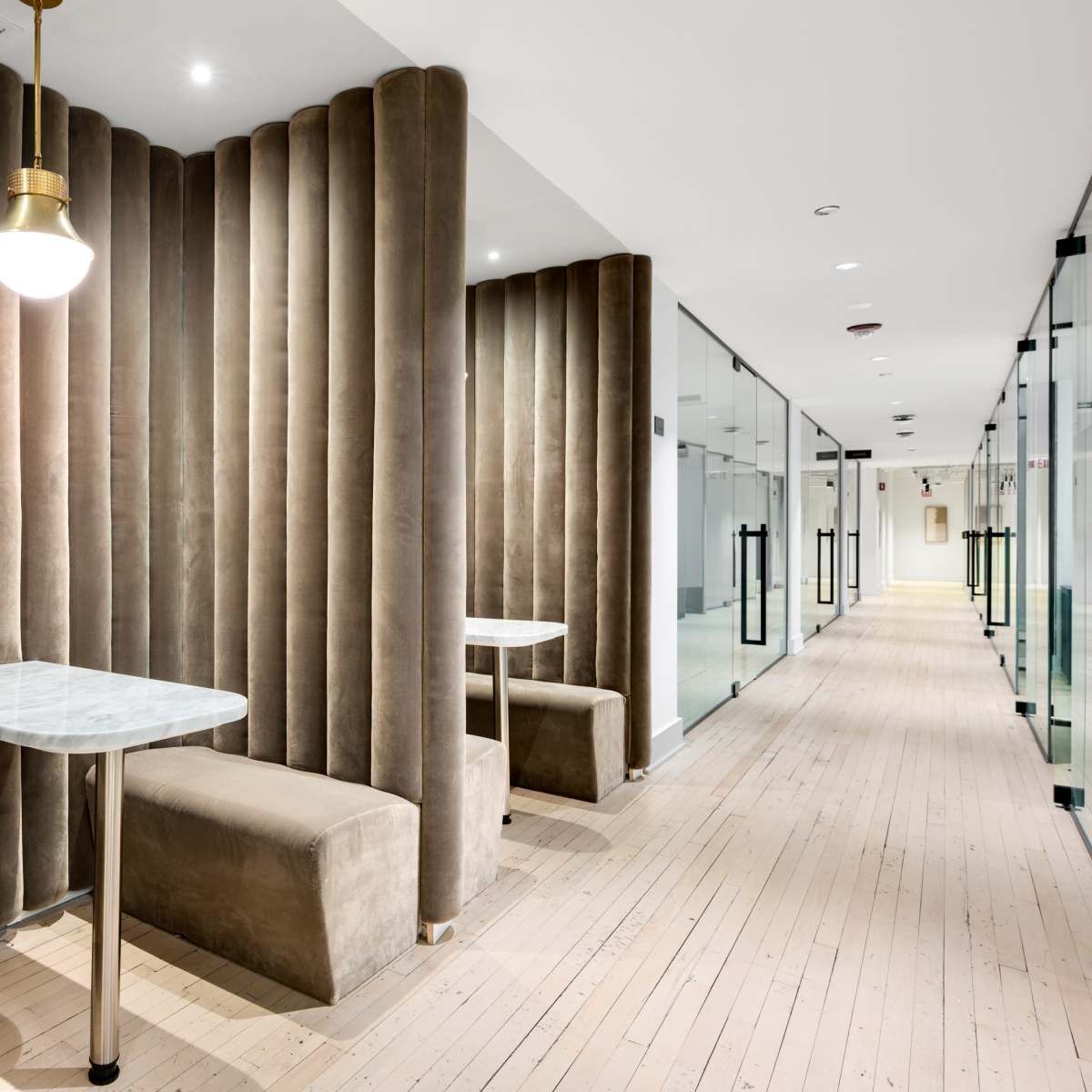 A narrow hallway featuring padded velvet walls, tables, and benches against one side, with glass partitions on the other side.