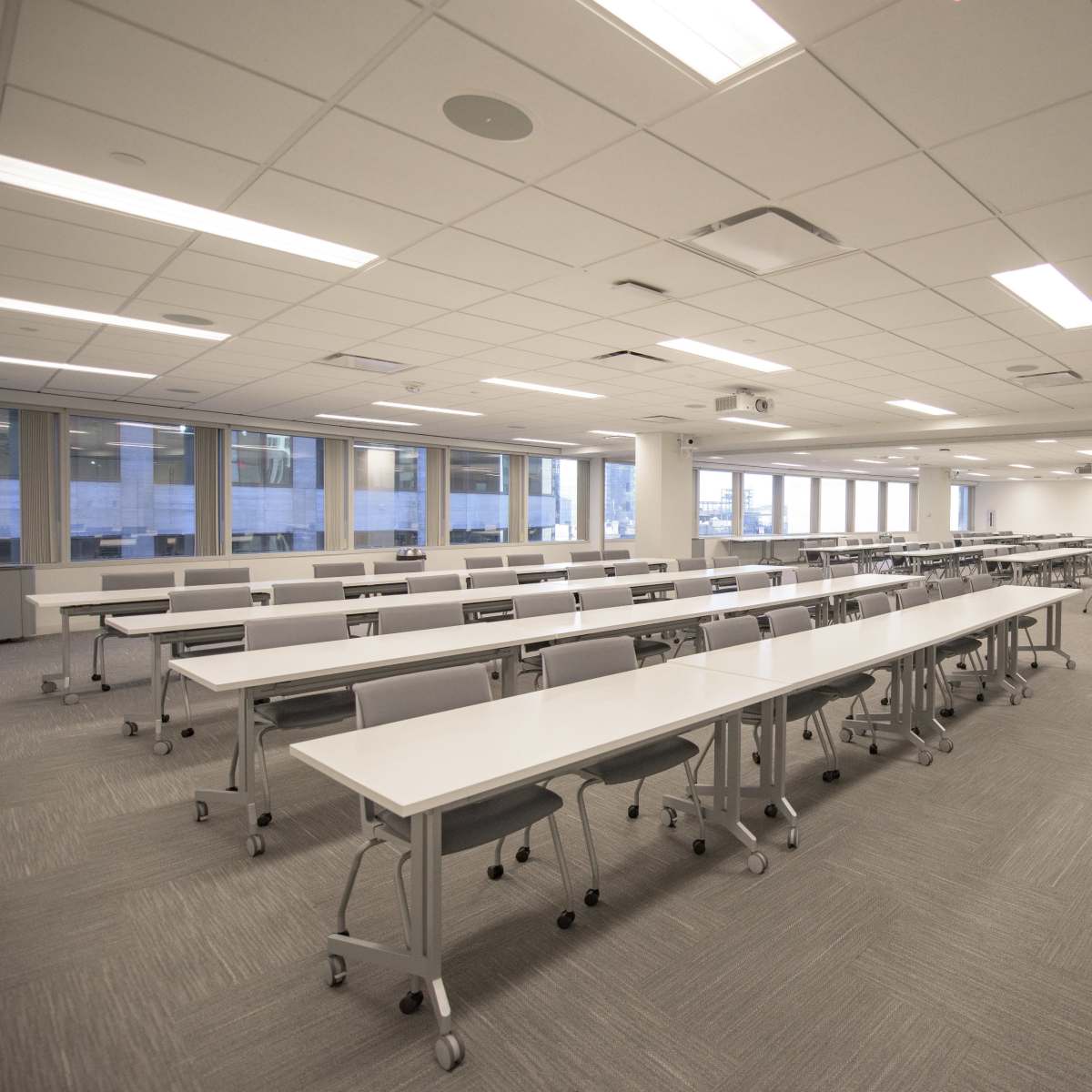 A spacious, well-lit classroom with multiple long tables and chairs arranged in a grid layout.
