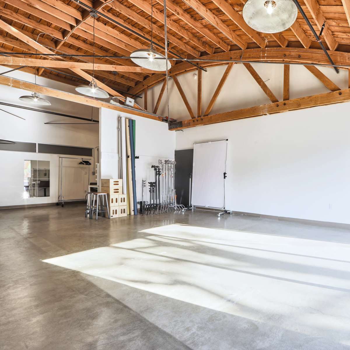 A spacious studio with high wooden beams, large windows, and concrete flooring, equipped with various photography gear.