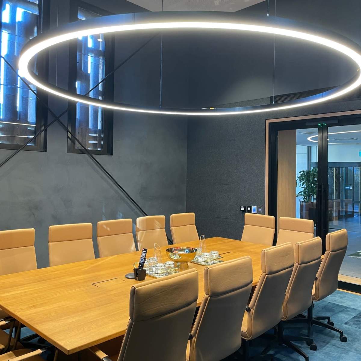 A modern conference room features a large wooden table surrounded by twelve leather chairs and an overhead ring light.