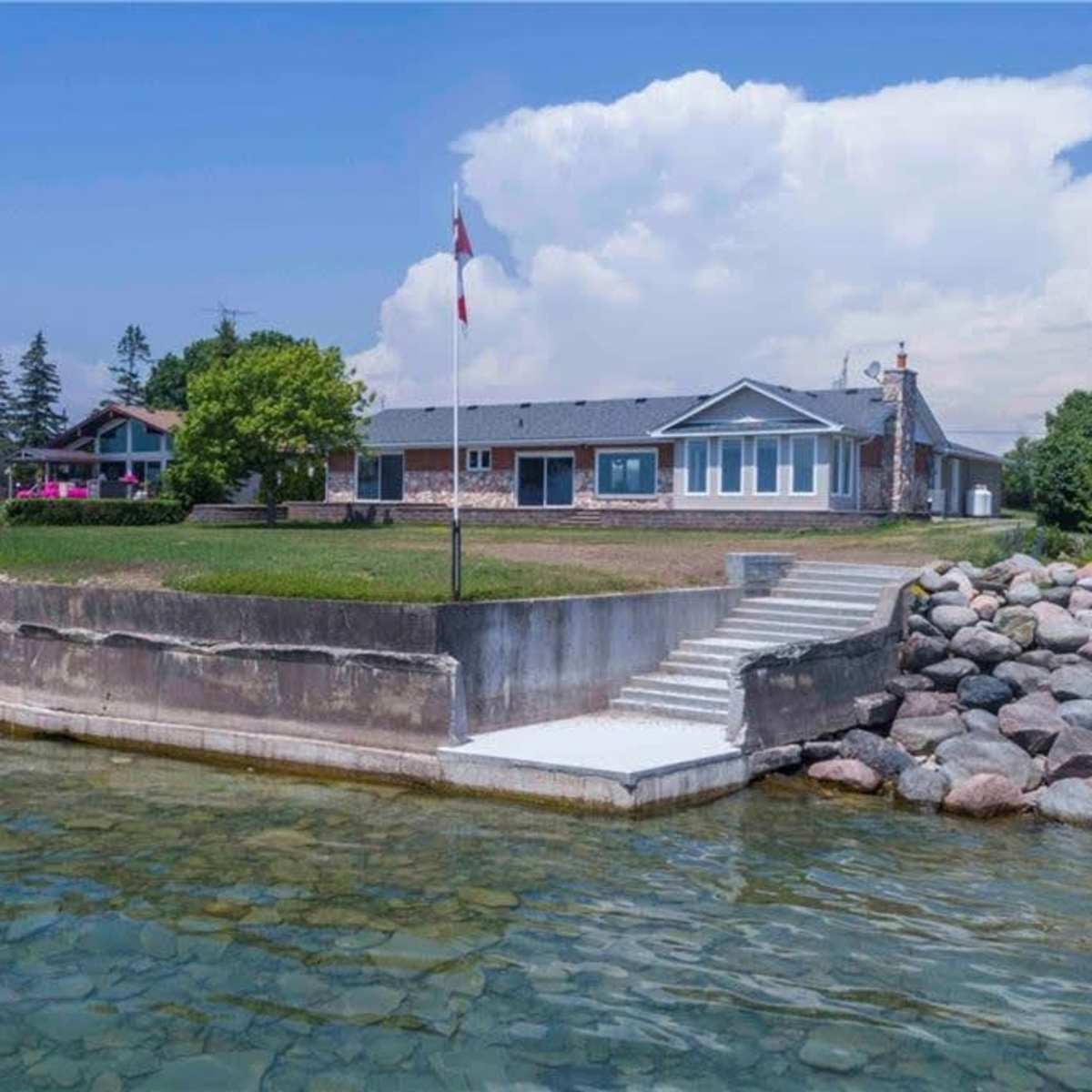 A lakeside property features a stone wall shoreline, a grassy area, and a building with multiple windows.