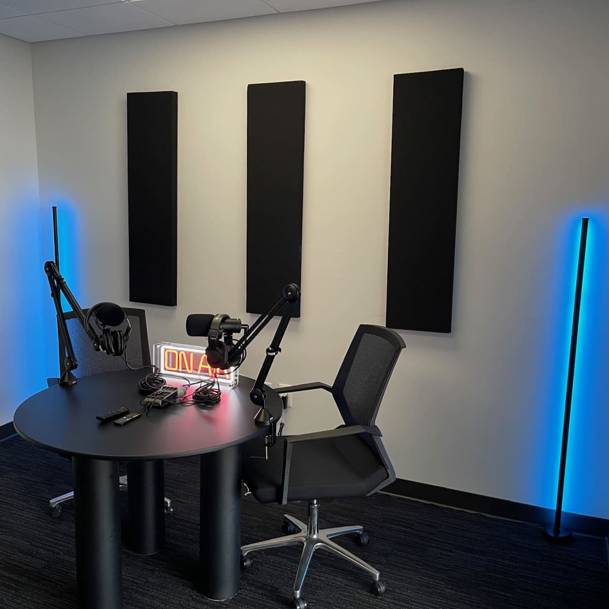 A soundproof recording studio with a round table, two microphones on adjustable arms, and neon lighting.