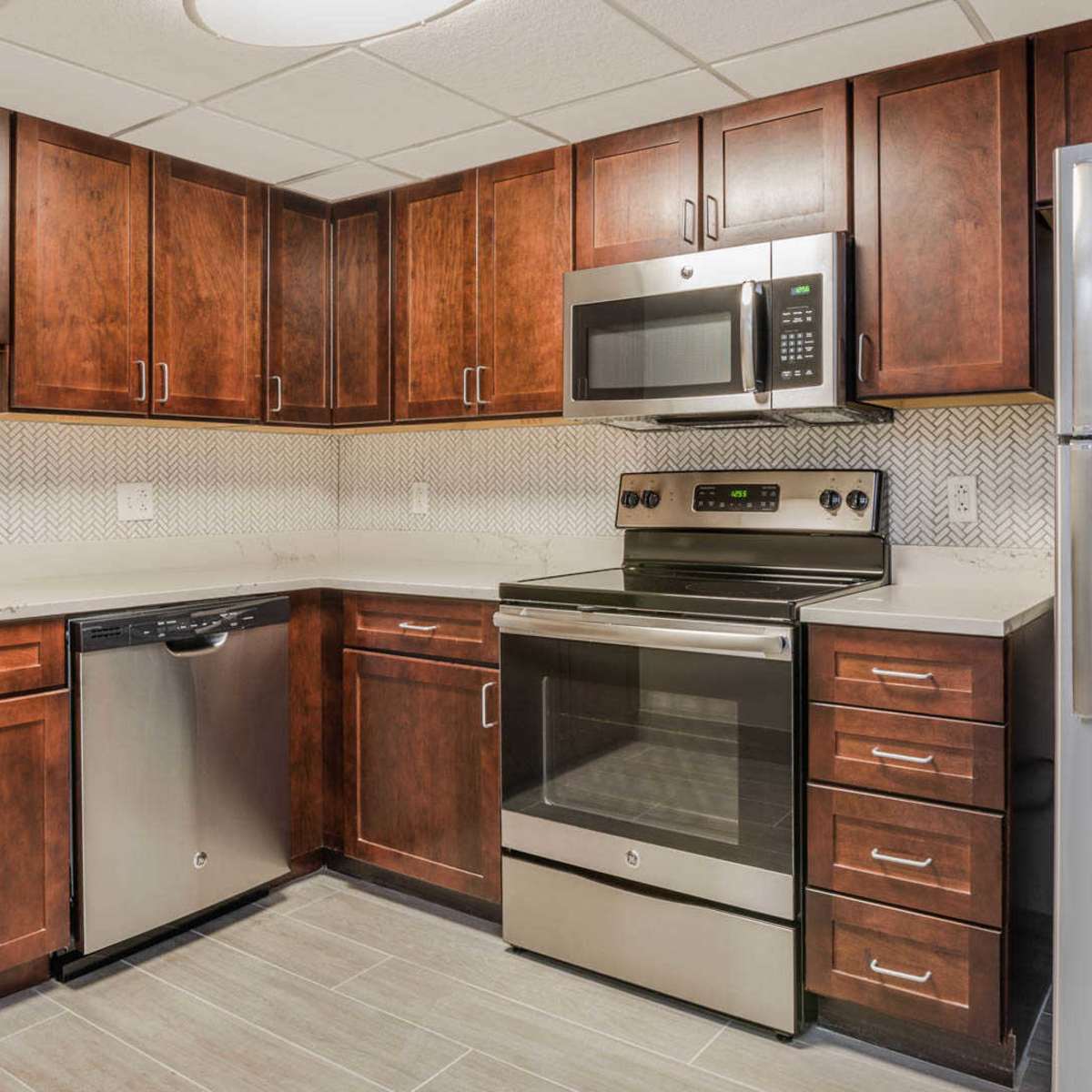 A modern kitchen with dark wooden cabinets, stainless steel appliances, and a neutral-toned tile backsplash.