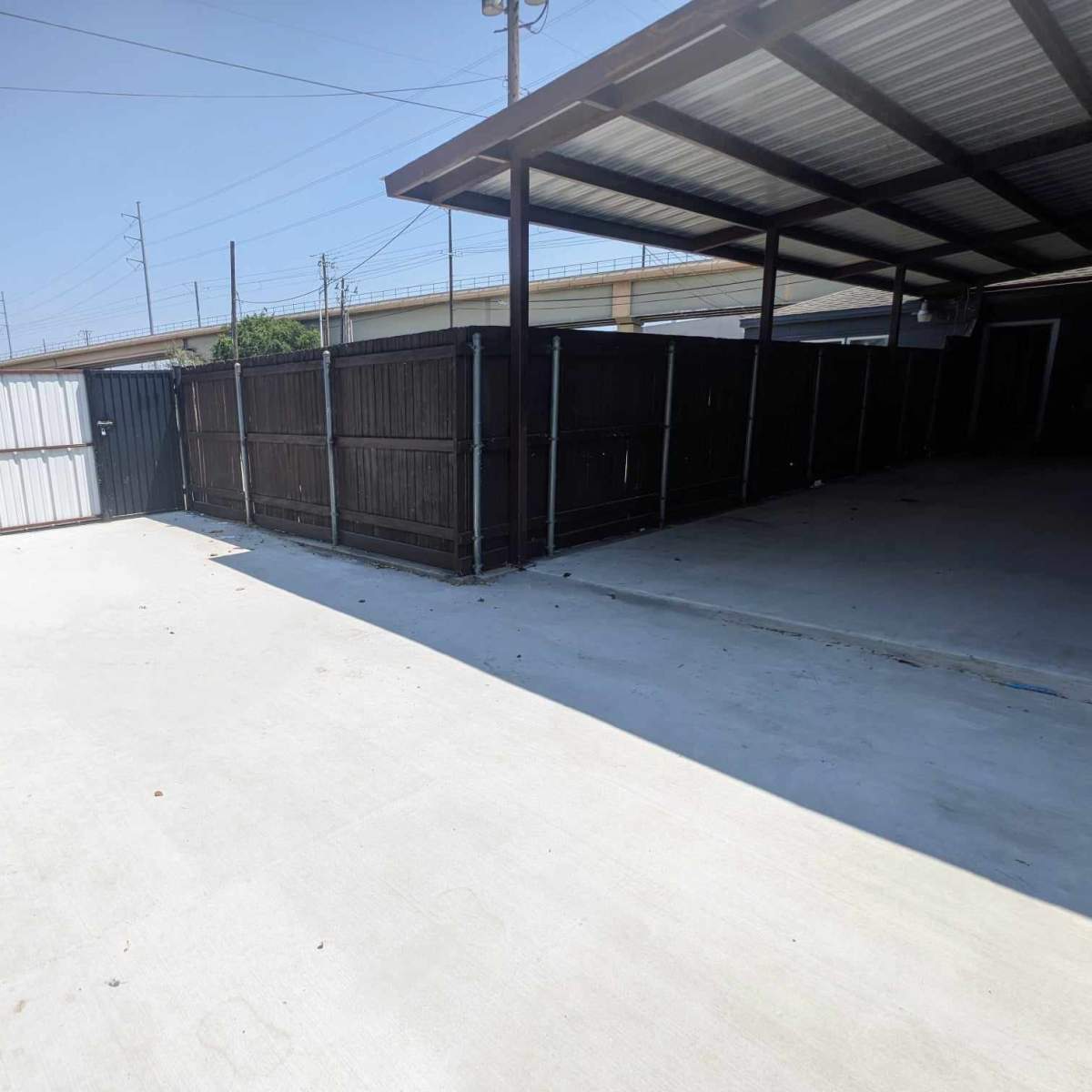 A concrete area enclosed by metal fencing and a covered structure, with a clear blue sky above.