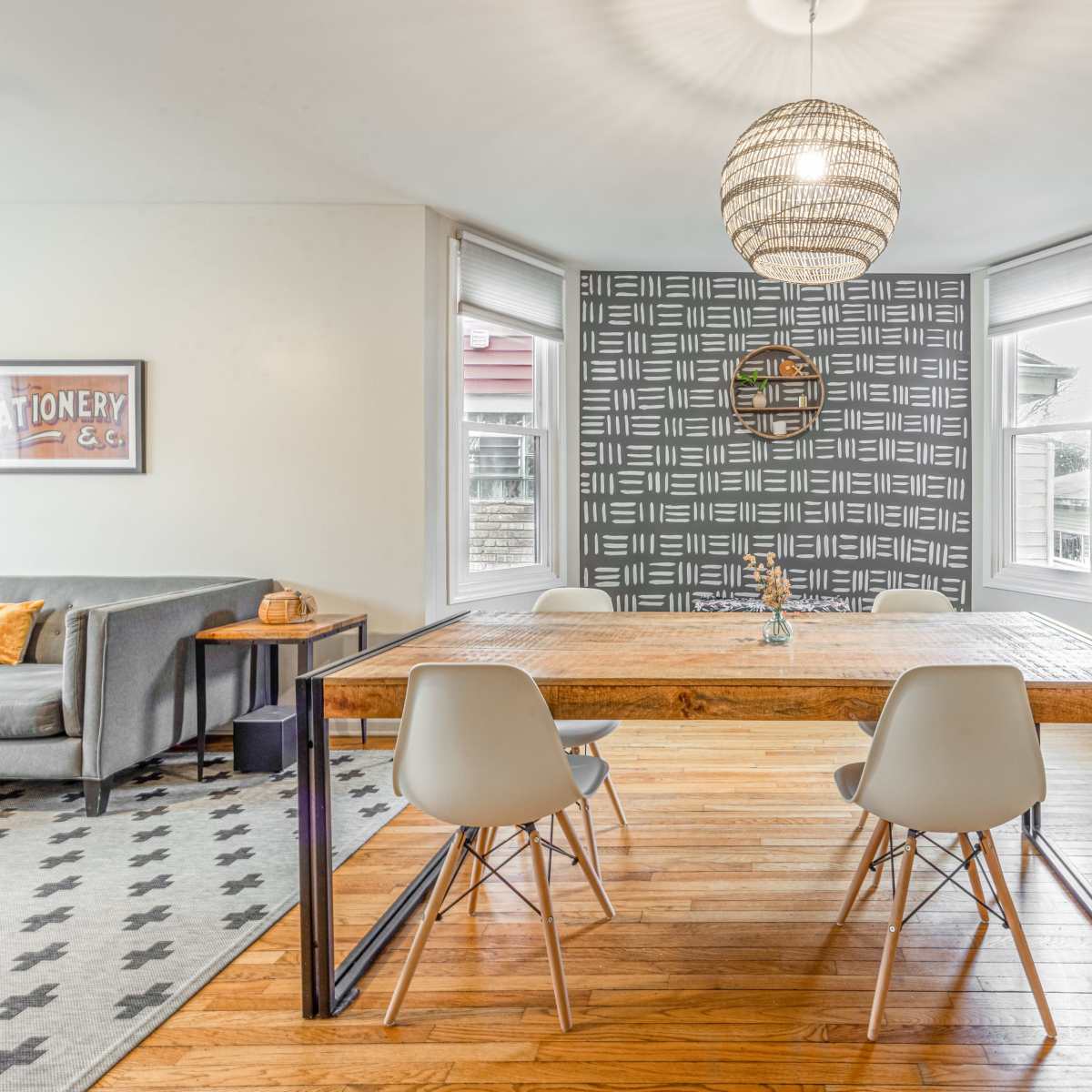 A modern dining area features a wooden table with metal legs and four white chairs, surrounded by large windows and a decorative wall pattern.