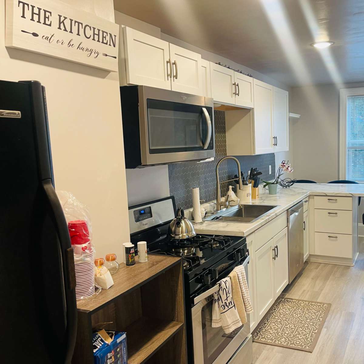 A modern kitchen features white cabinetry, stainless steel appliances, and a dining area with large windows.