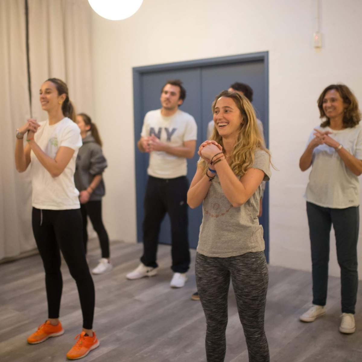 A group of seven people are participating in a movement or exercise class in a brightly lit room.