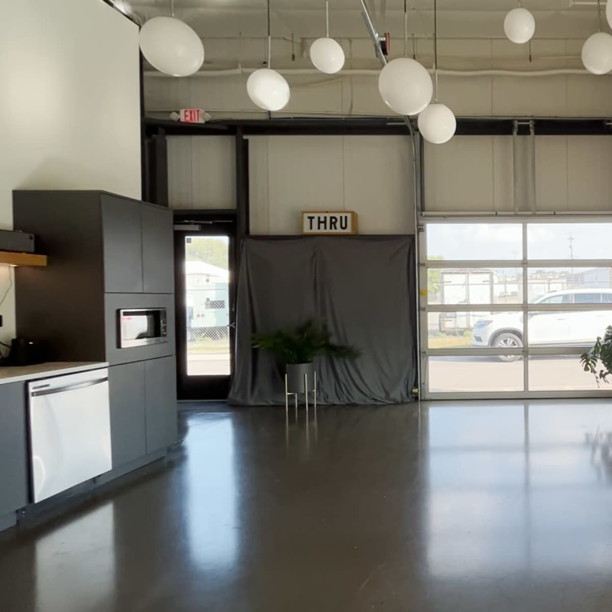 An interior space with modern decor, featuring a small kitchen area, a living area with a sofa, and large windows letting in natural light.