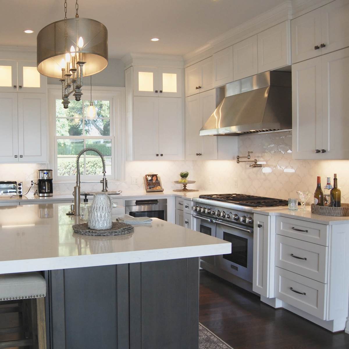 A modern kitchen features white cabinets, a large island with bar stools, stainless steel appliances, and a chandelier overhead.