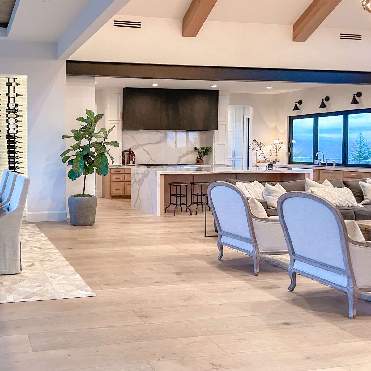 An open-concept living area featuring a dining table with chairs, a kitchen with a large island, and a display of wine bottles on the wall.