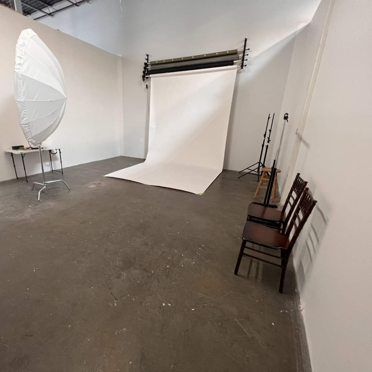 A photography studio with a white backdrop, a large softbox light, and several chairs arranged along the side.