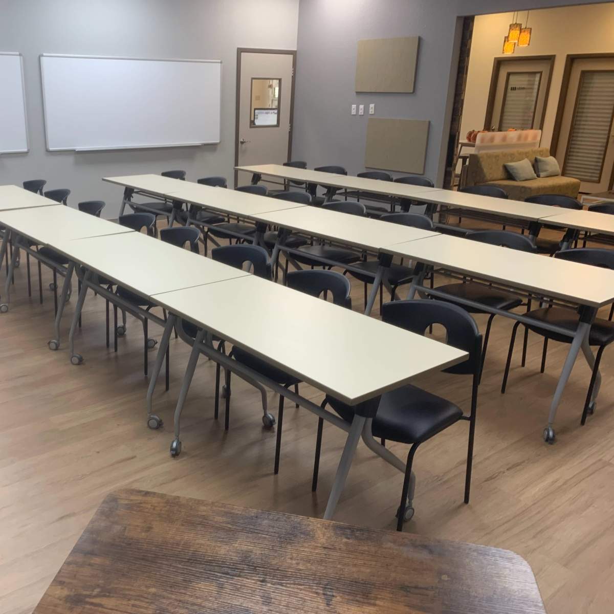 A classroom with multiple rows of tables and chairs facing a front area equipped with whiteboards.