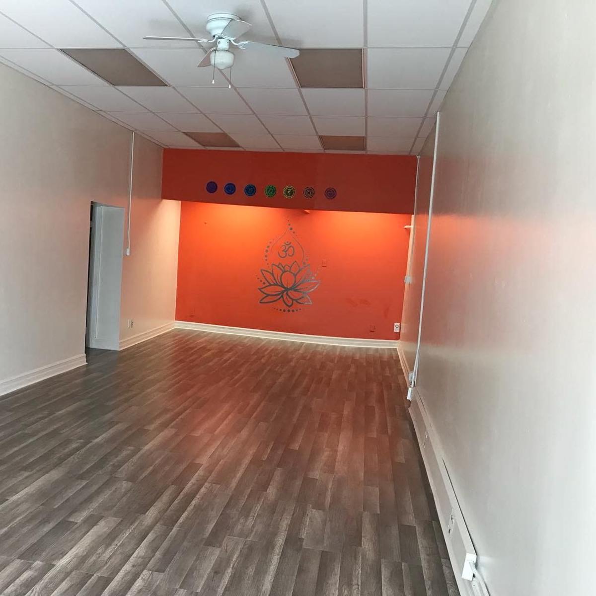 A spacious room with light-colored walls, a lotus flower mural on an orange accent wall, and a wooden floor.