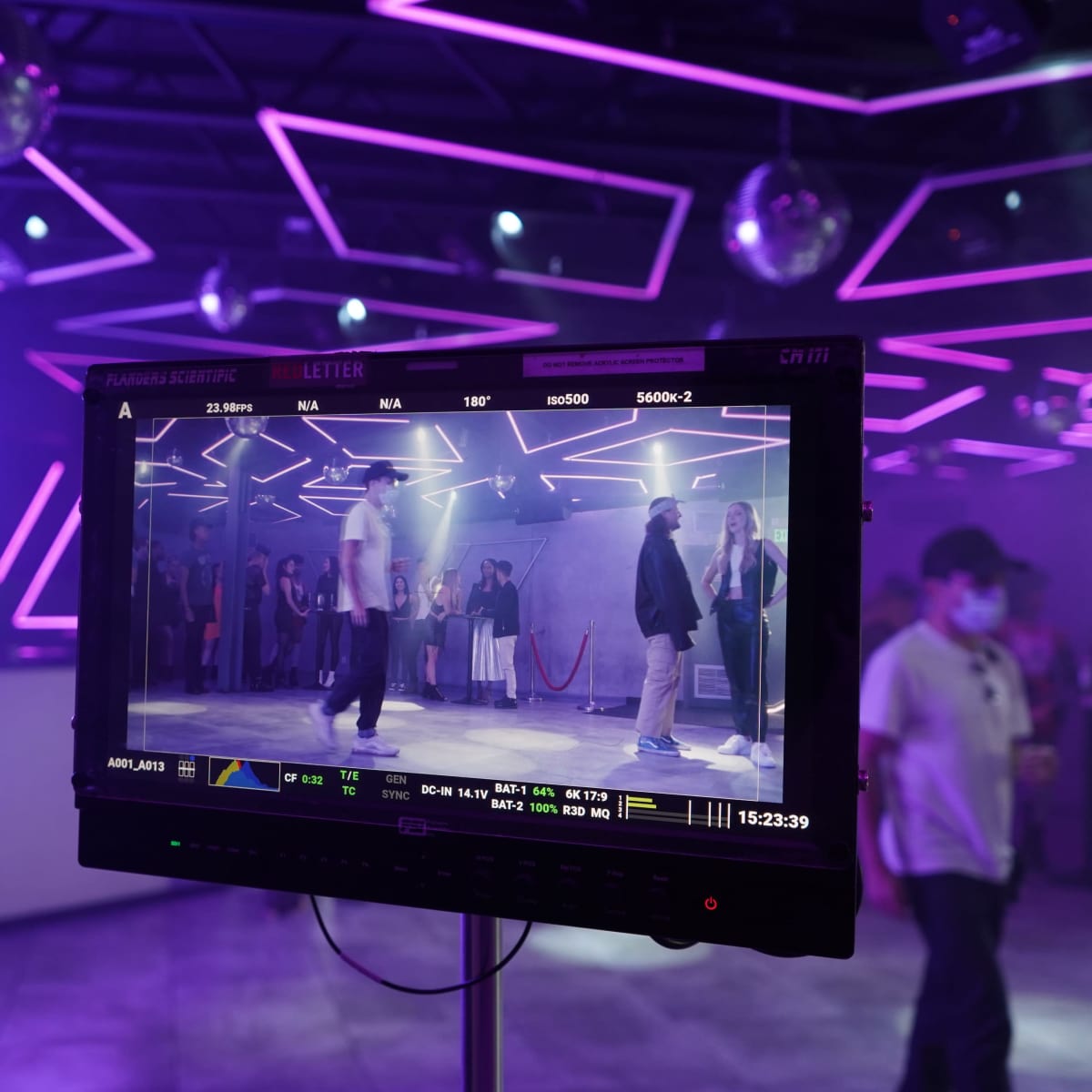 A monitor displays a scene of performers dancing in a venue with purple lighting and disco balls.