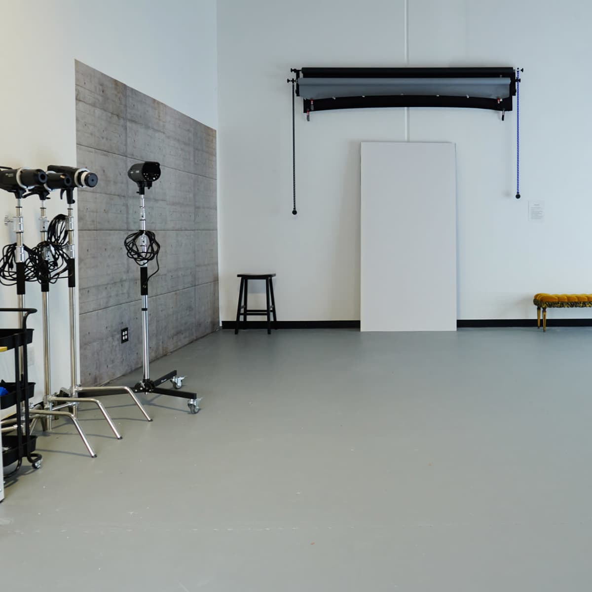 A spacious photography studio with various lighting equipment, a backdrop, and a decorative bench against a plain wall.
