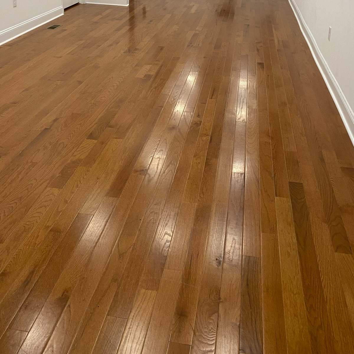 A spacious room with hardwood flooring, white walls, and recessed lighting.