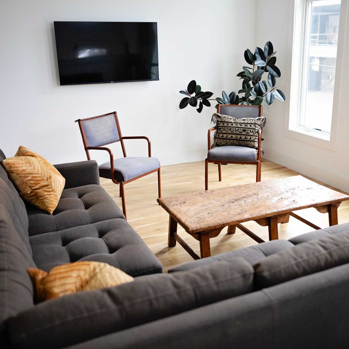 A modern living room featuring a gray sofa, two chairs, a wooden coffee table, and a large television mounted on the wall.