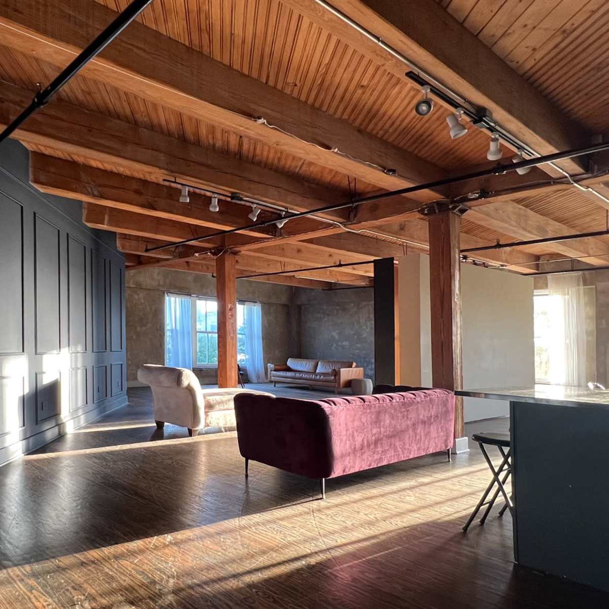 A spacious room with wooden beams, a gray wall, and various seating arrangements, including a purple couch and chairs.