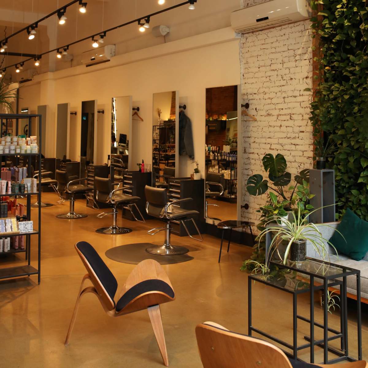 A modern hair salon interior with styling chairs, large mirrors, and a wall covered in greenery.