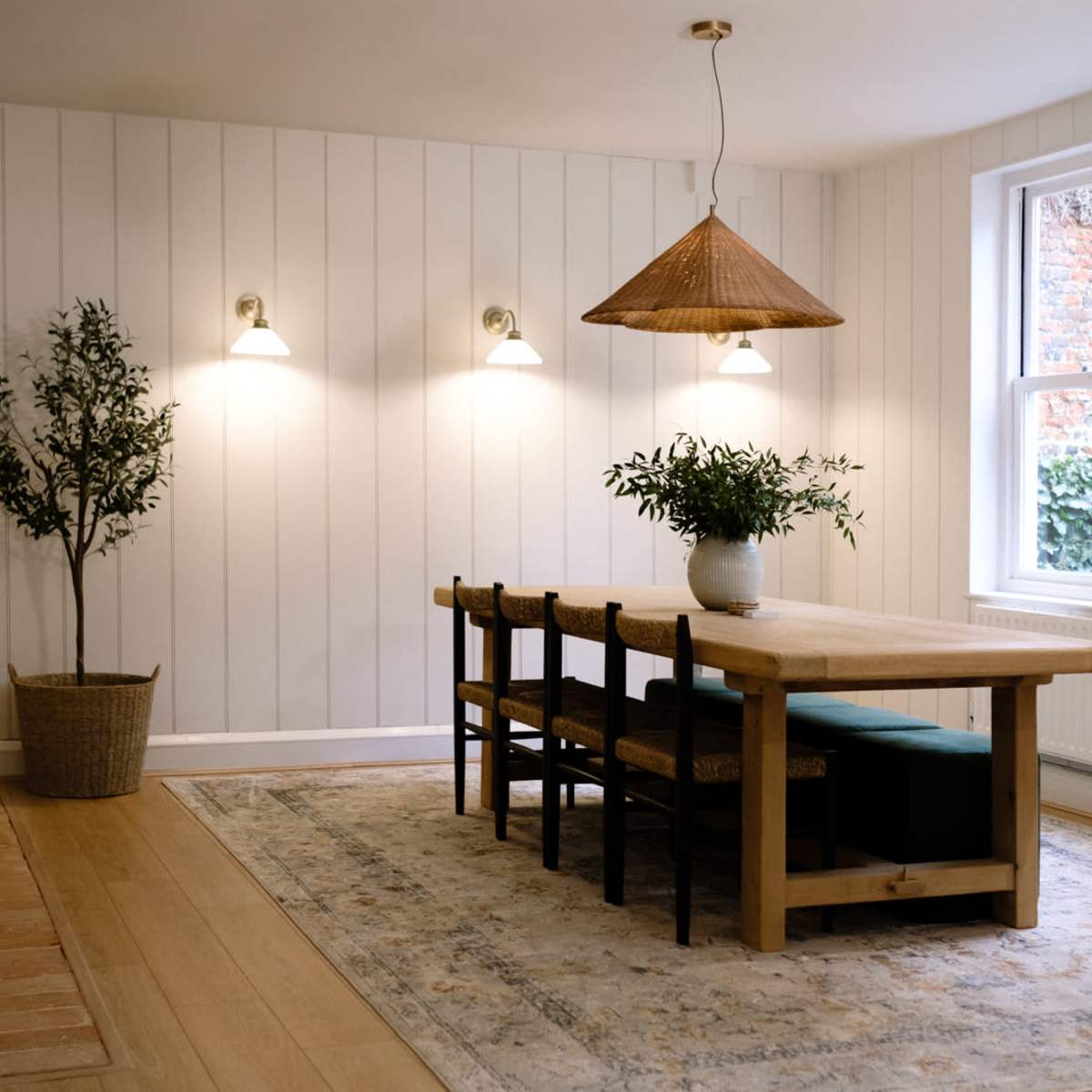 A spacious dining room features a wooden table surrounded by chairs, a hanging light fixture, and a potted plant in the corner.