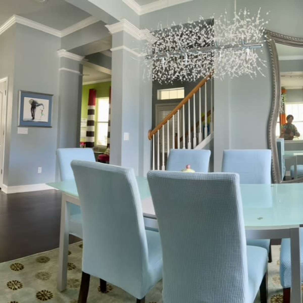 A dining area with a light blue table and chairs, a large mirror, and large windows allowing natural light to fill the space.