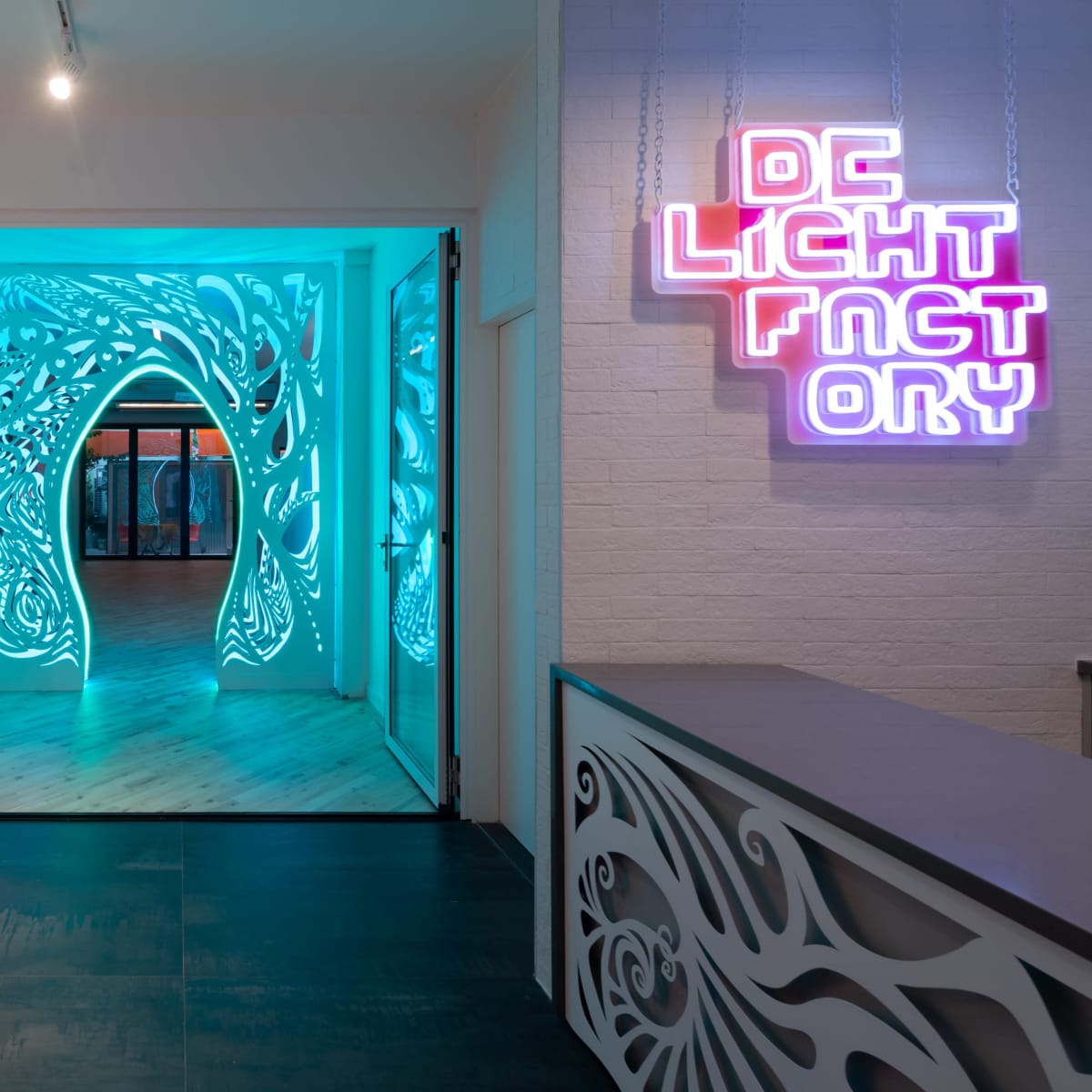 A brightly lit interior space with colorful wall panels and a neon sign that reads "DC LIGHT FACTORY," leading to an intricately designed archway.