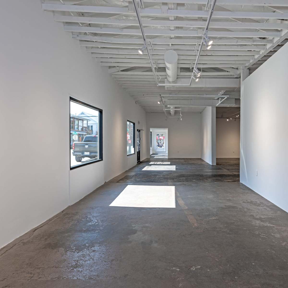 A spacious, empty art gallery with large windows and polished concrete floors.