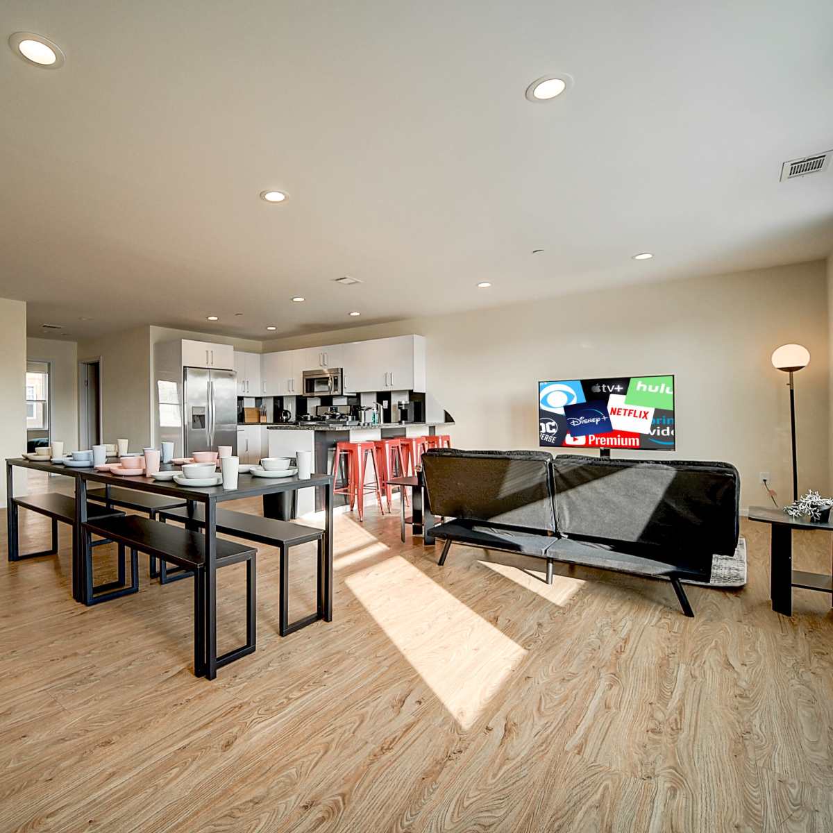 A modern open-concept living area with a dining table set for several people, a couch, and a kitchen in the background.
