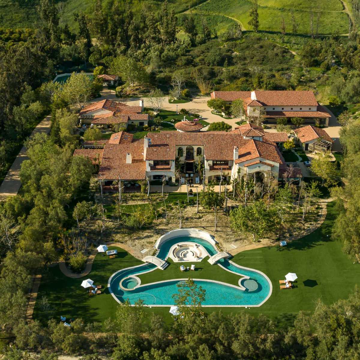 An aerial view of a large estate featuring several buildings, a landscaped lawn, and a swimming pool.
