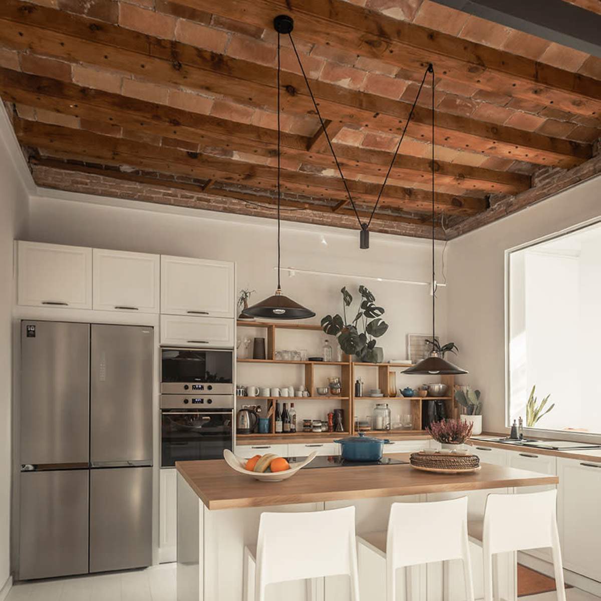 The kitchen features a central island with seating, stainless steel appliances, and wooden ceiling beams.