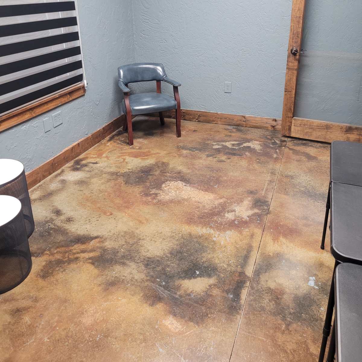 A sparsely furnished room with a single chair, a glass-panel door, and two small tables on a stained concrete floor.