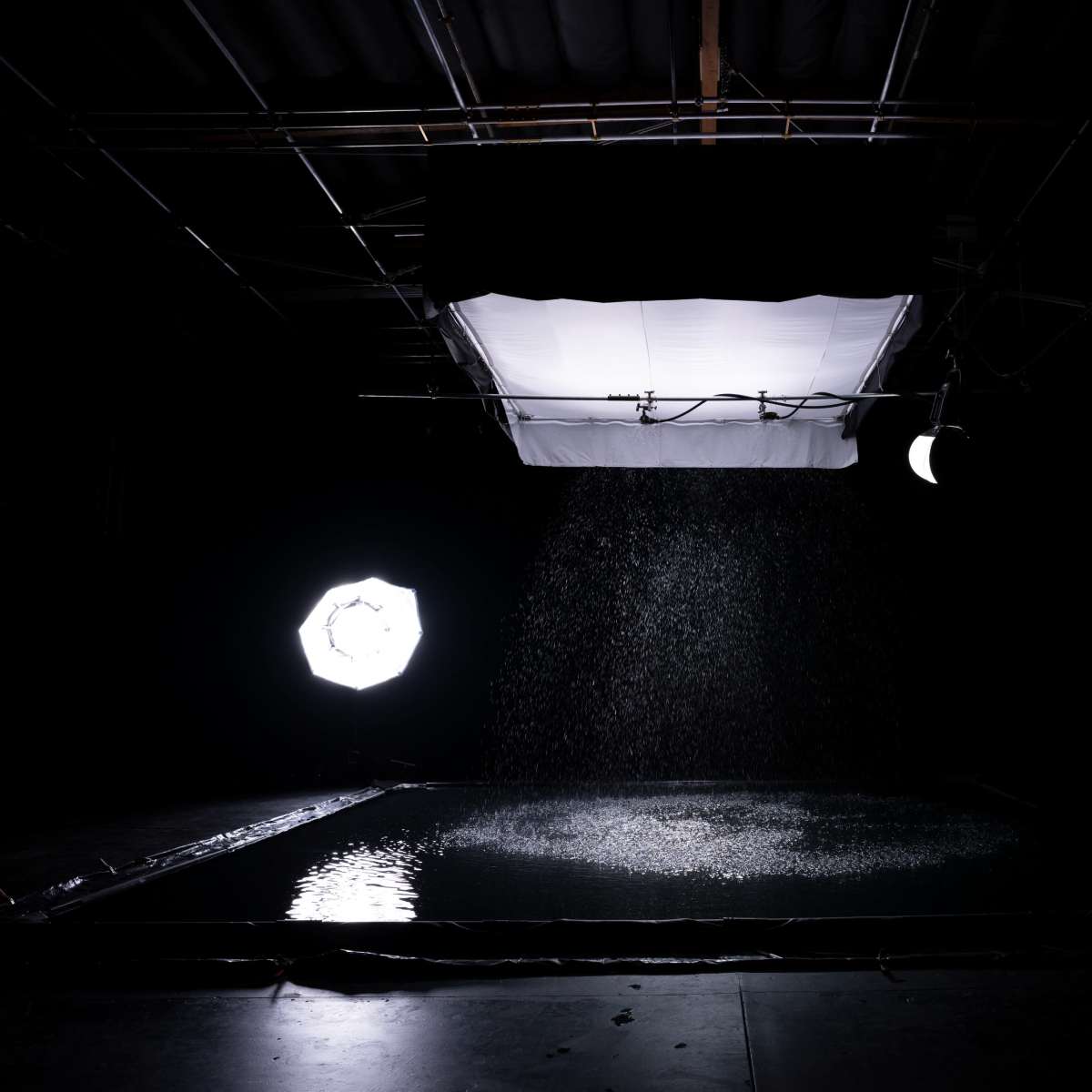 A dark studio setup with a water-covered surface, illuminated by a softbox and a circular light source.