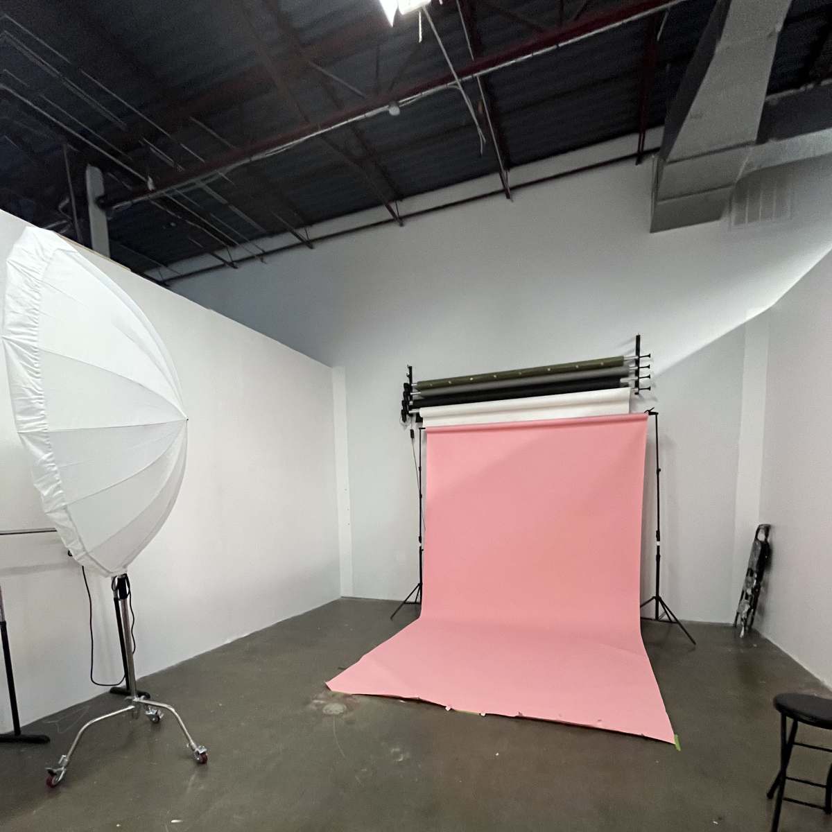 A photography studio with a pink backdrop, a large light modifier, and minimal furniture.