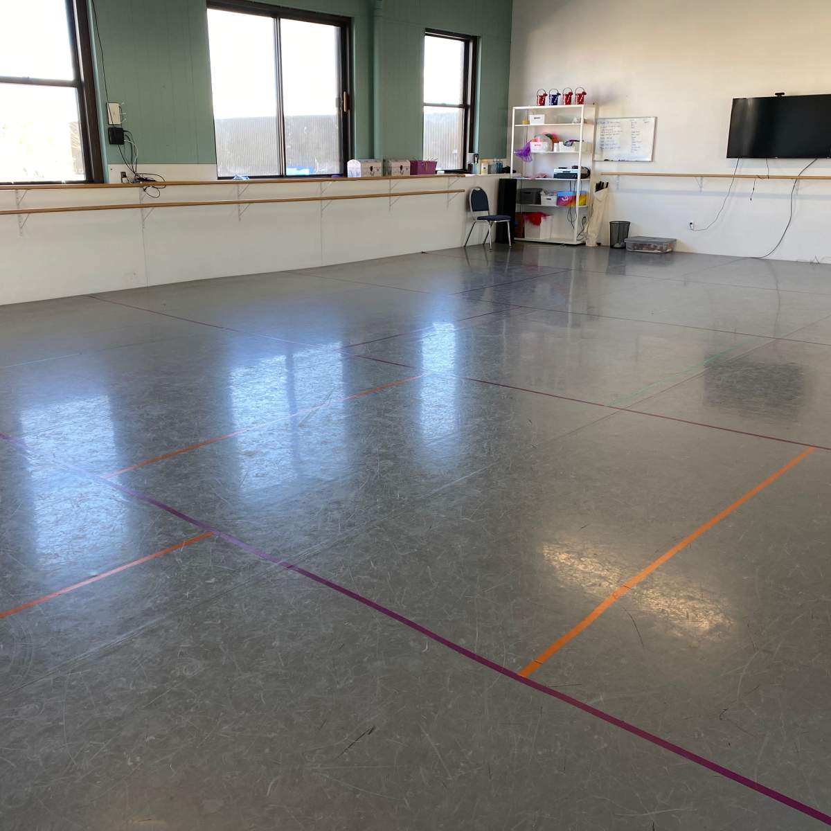 A spacious dance studio with a smooth floor marked by colored lines and a small seating area along one wall.