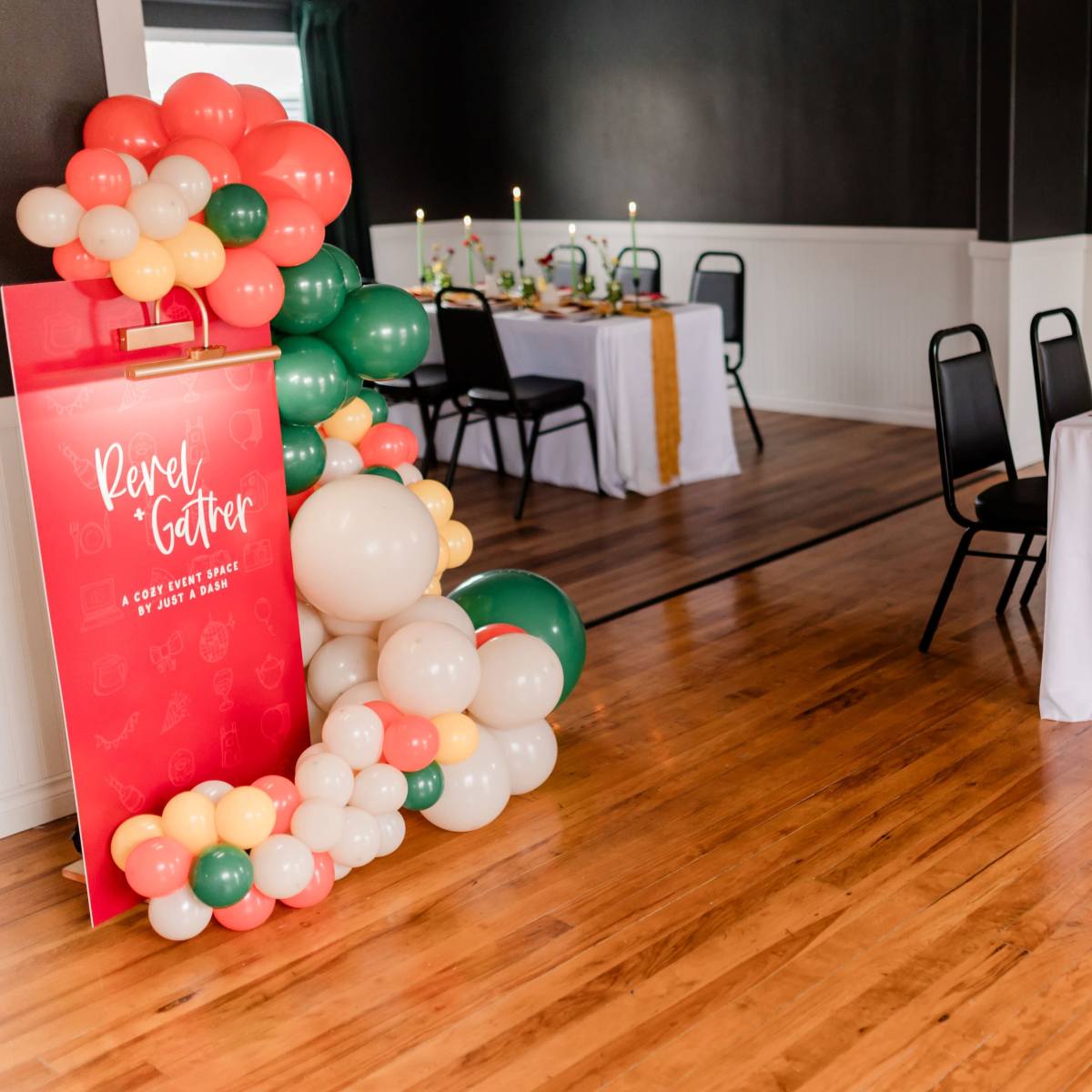 A decorated dining area with two long tables set for a meal, surrounded by balloons and a sign featuring the words "Revel Gather."