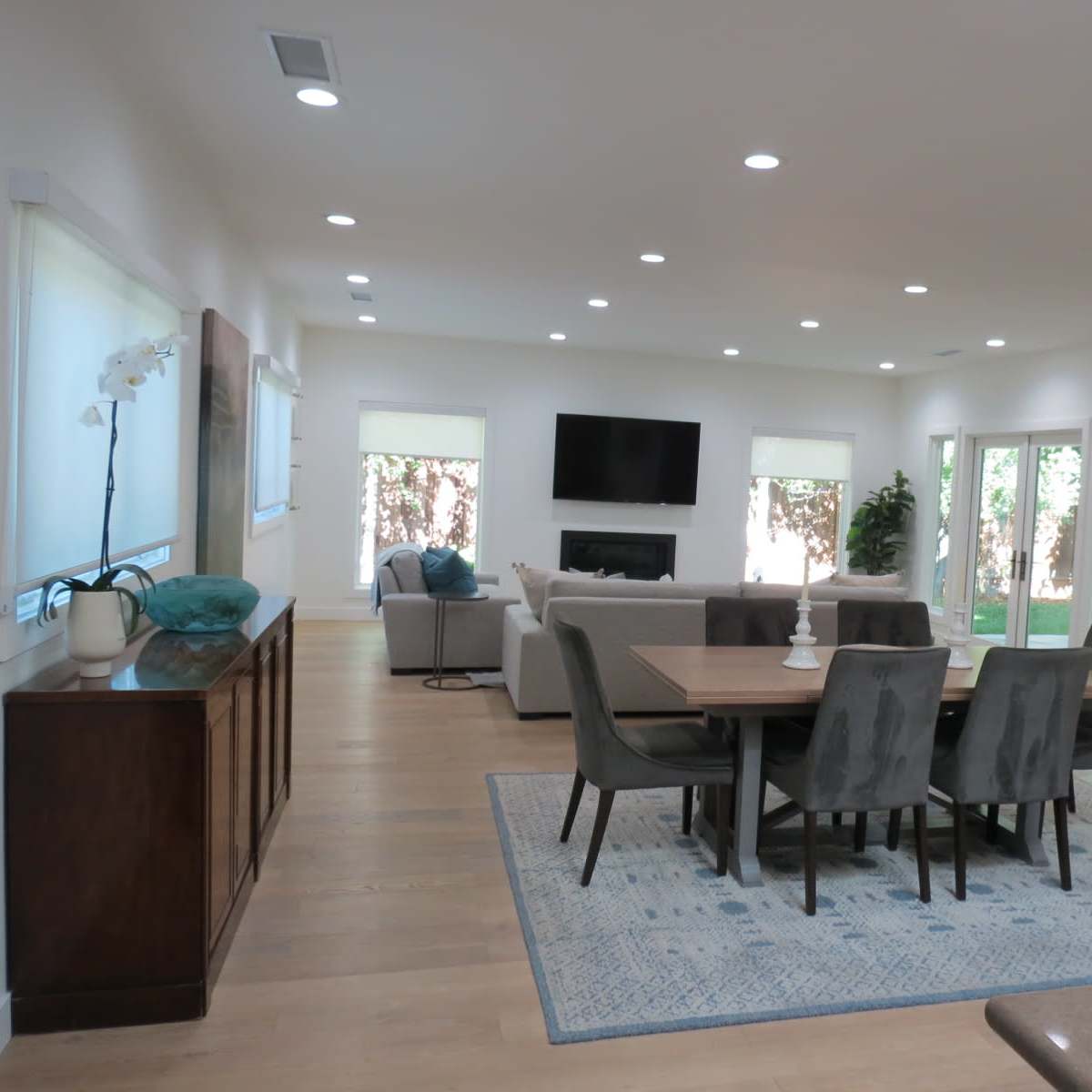 A modern, open-concept living and dining area featuring a dining table surrounded by chairs, a lounge area with a couch, and large windows leading to a backyard.