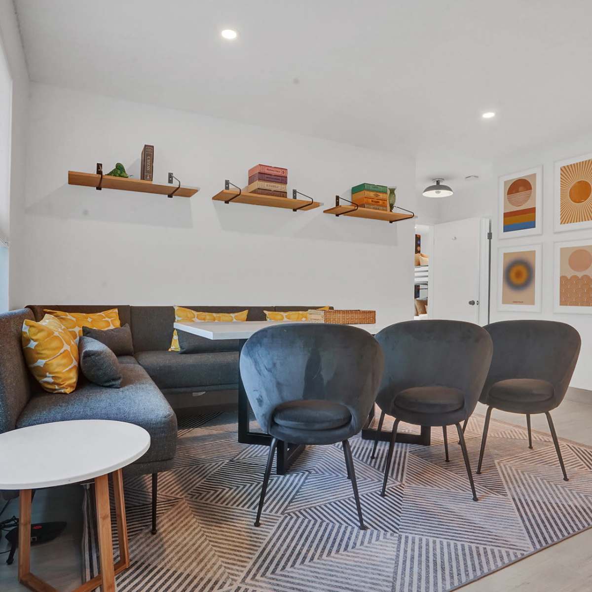 A modern living area with a gray sofa, four black chairs arranged around a patterned rug, and colorful artwork on the wall.