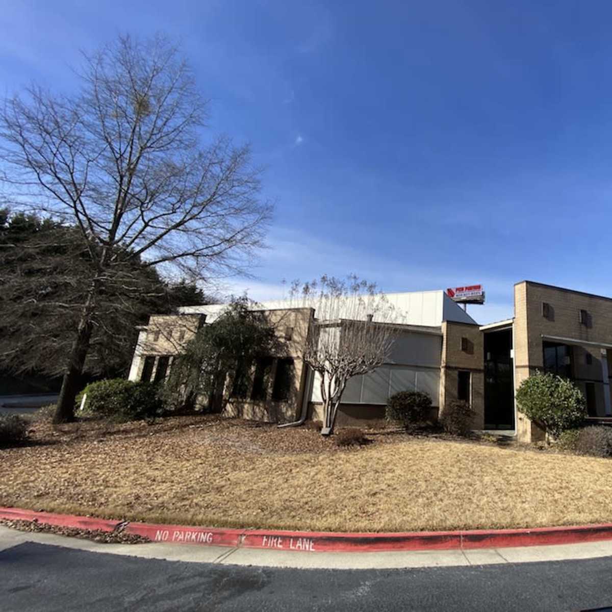 A two-story commercial building with a tan exterior and landscaped grounds is visible on a sunny day.