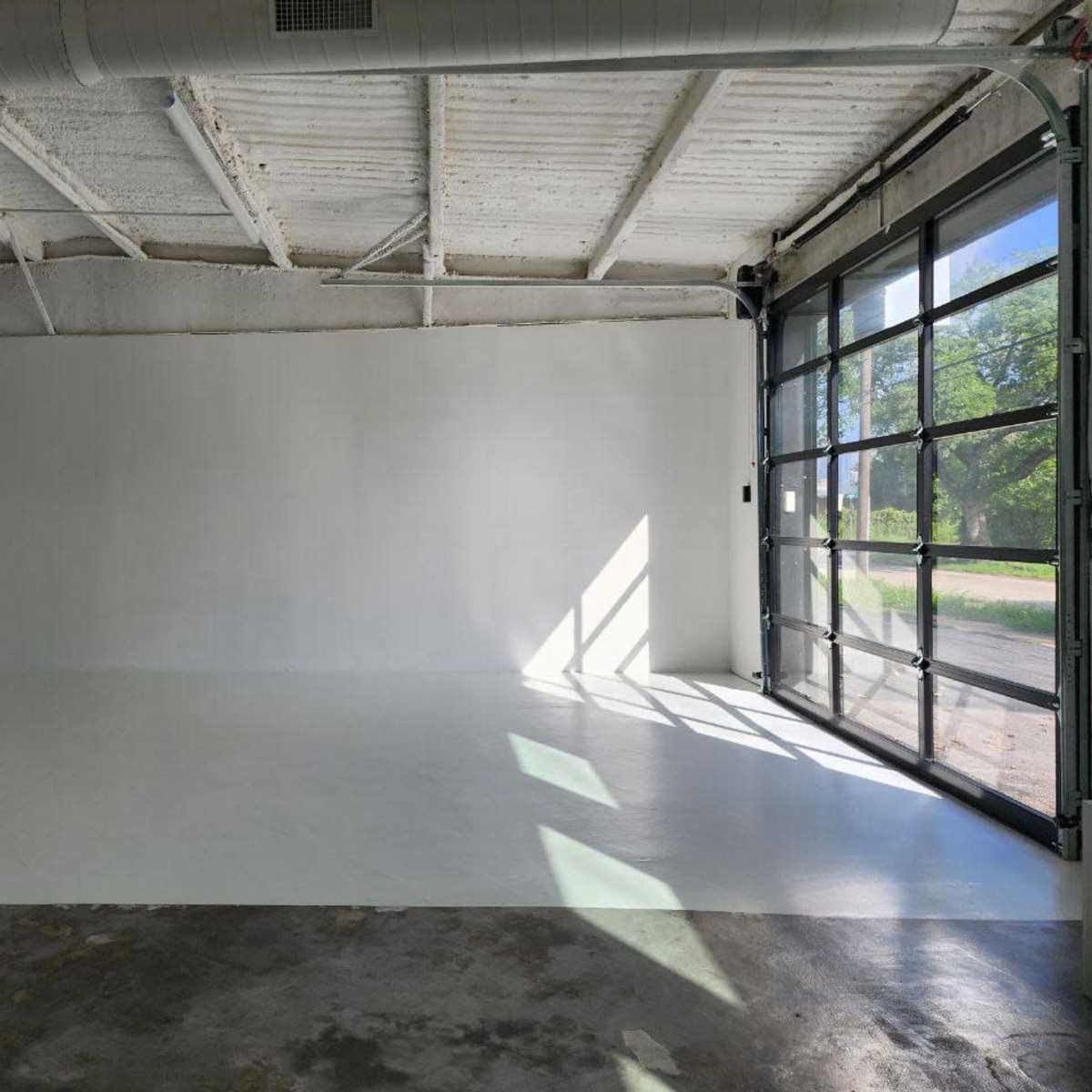 A spacious, empty room with a glossy white floor and a large glass garage door allowing natural light to enter.