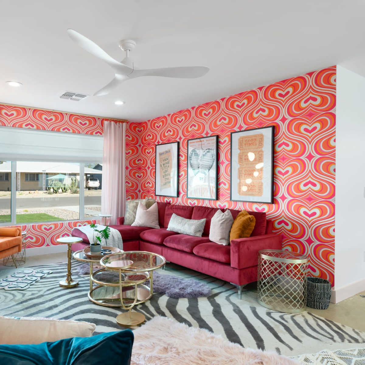 The living room features a vibrant pink heart-patterned wall, a red sofa, and a mix of colorful decor elements, including a zebra-striped rug and modern furniture.