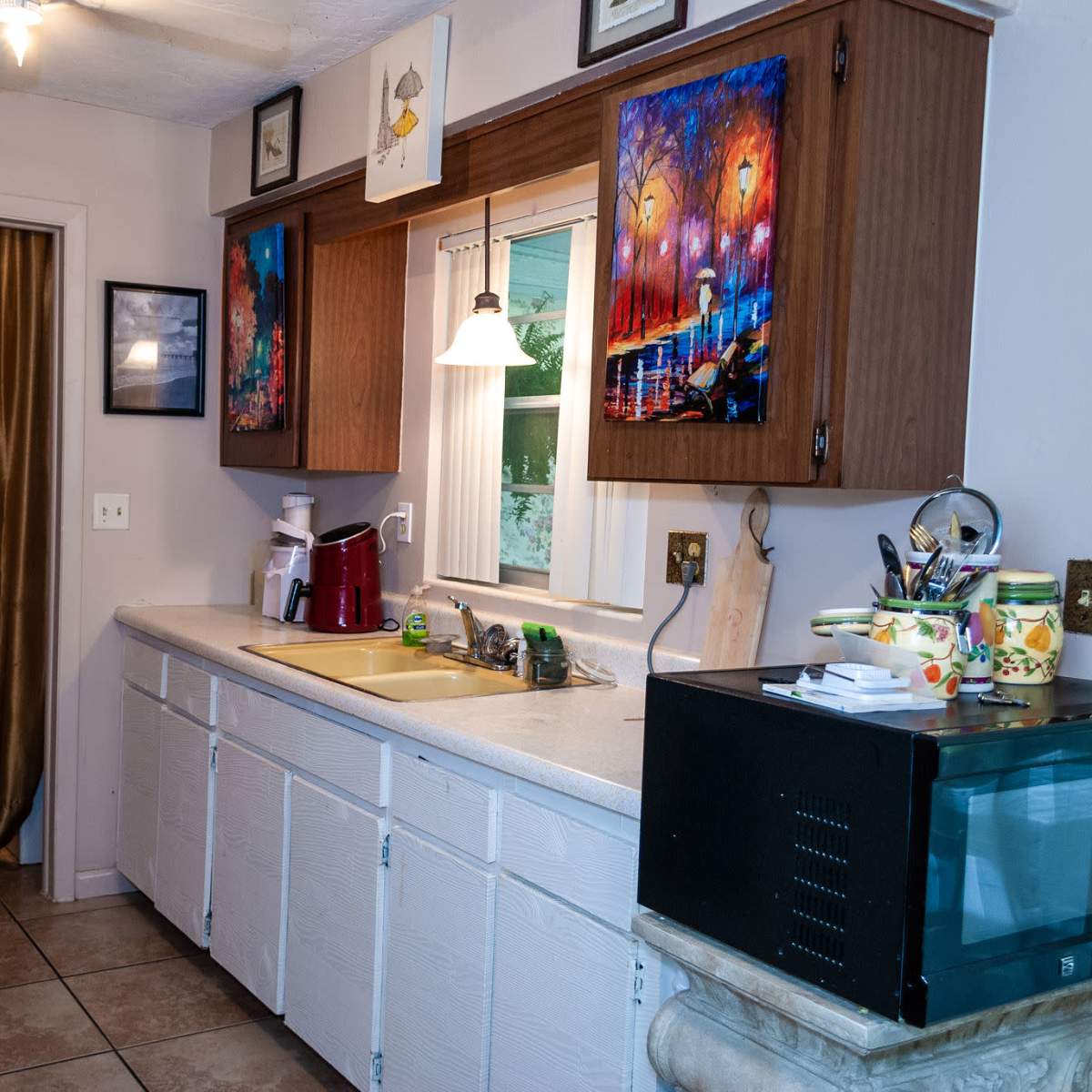 A kitchen with white cabinets, a sink beneath a window, a countertop with a coffee maker, and a microwave on the right side.