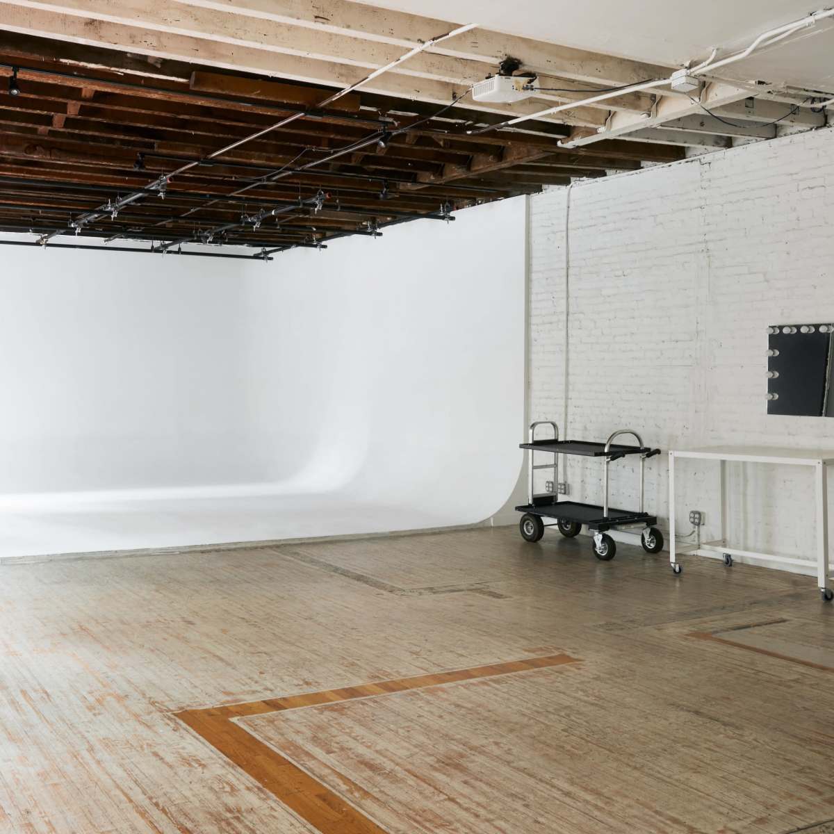 A spacious photography studio with a white backdrop, wooden floors, and natural light coming through a window.