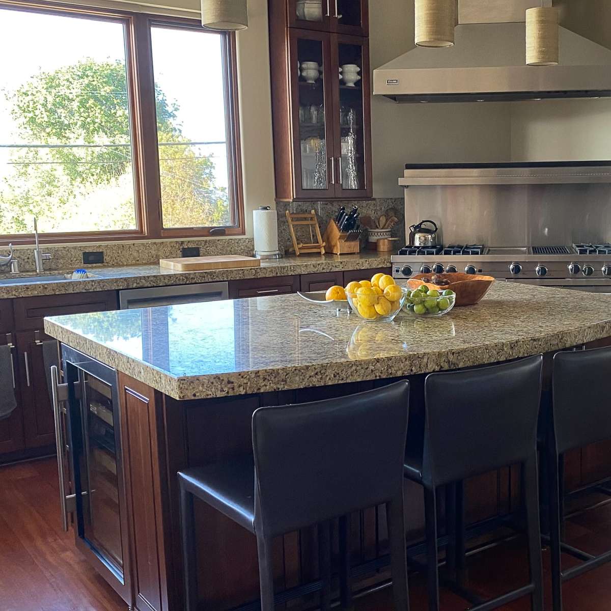 The kitchen features a central island with bar stools, granite countertops, stainless steel appliances, and large windows that provide natural light.