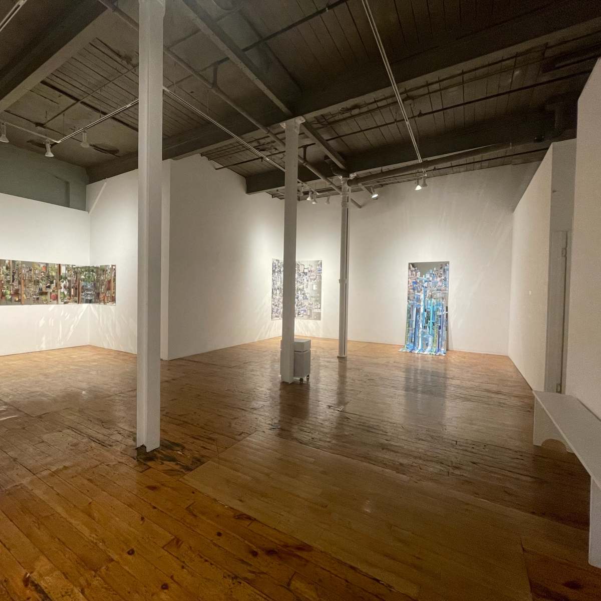 An art gallery with wooden floors, featuring two wall installations and a doorway framed by transparent materials.