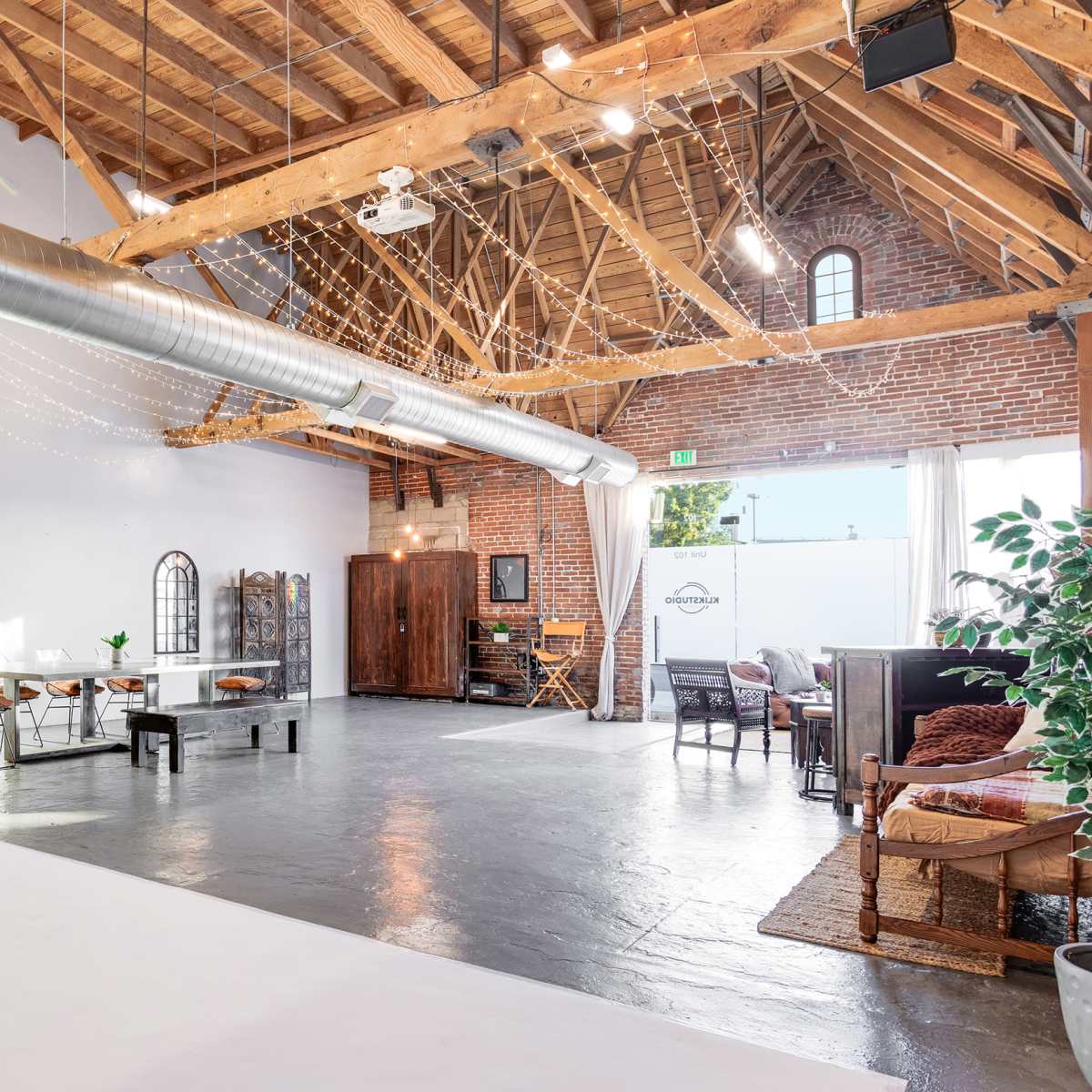 A spacious interior room with exposed wooden beams, brick walls, and various seating arrangements, including a table and chairs.
