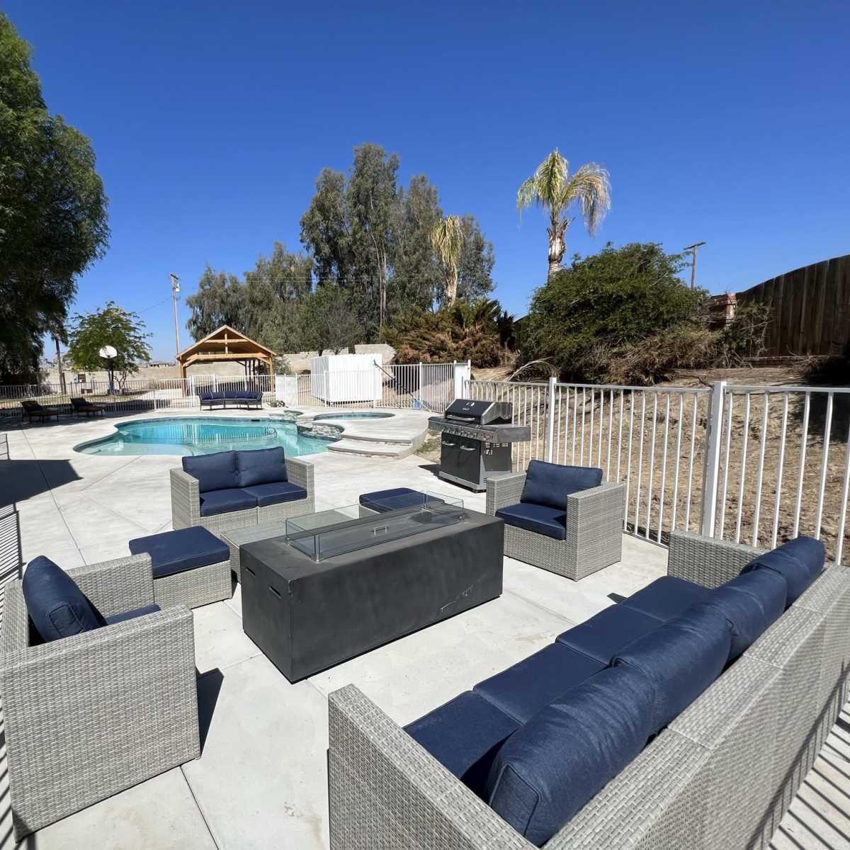 A patio area with outdoor furniture surrounding a swimming pool, enclosed by a white fence.
