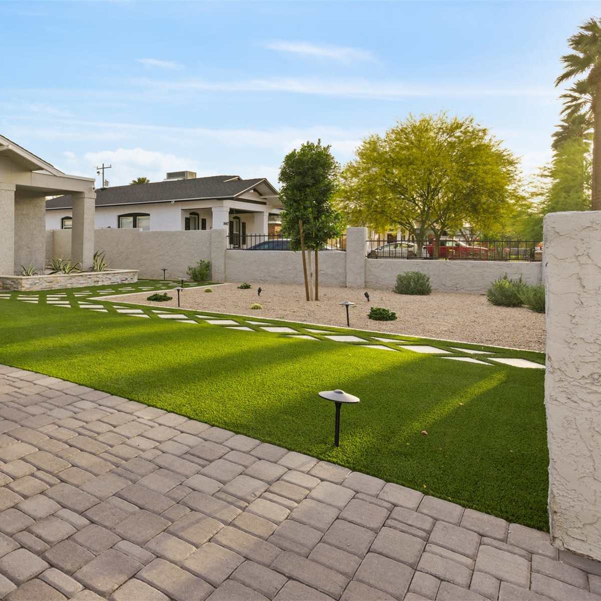A modern house with a paved driveway features a landscaped front yard with artificial grass and a gravel area.